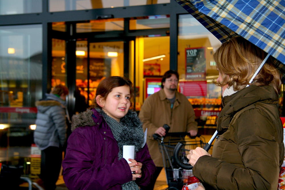 Eine Teilnehmerin spricht Einkäufer an, ob sie ein Kilo mehr Lebensmittel für Benachteiligte kaufen möchten.